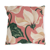 Floral outdoor pillow with large painted cream cyclamen flowers and dark green leaves on coral pink