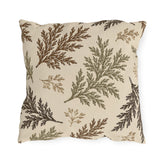 Cedar sprigs in brown, olive and tan scattered on a cream outdoor pillow