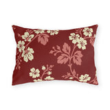 Cream blossoms on rose branches over a deep brick red outdoor lumbar pillow