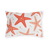 Coastal outdoor lumbar pillow with tossed coral and peach starfish and sandy dots on white