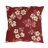 Cream blossoms on rose branches over a deep brick red outdoor pillow