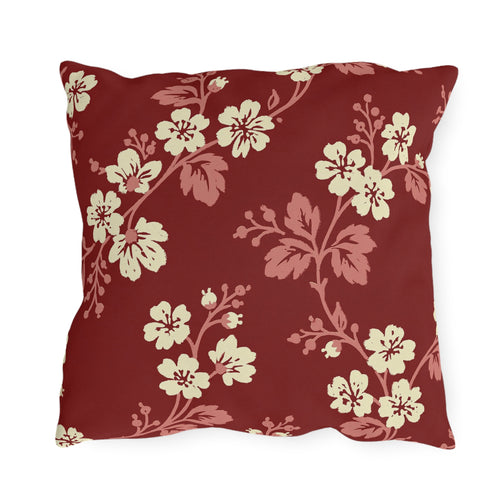 Cream blossoms on rose branches over a deep brick red outdoor pillow