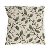 White snowberries on brown branches with green leaves on a cream outdoor pillow