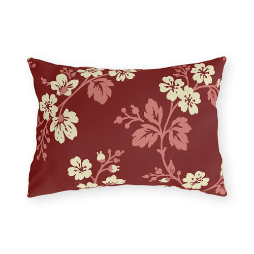 Cream blossoms on rose branches over a deep brick red outdoor lumbar pillow
