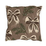 Cream and chocolate bows with spruce sprigs on a warm brown outdoor pillow