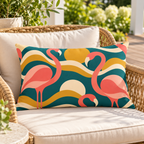 Teal retro flamingo outdoor lumbar pillow styled on a rattan lounge chair on a sunny deck