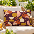 Plum mid-century flamingo outdoor lumbar pillow styled on a rattan lounge chair on a sunny deck