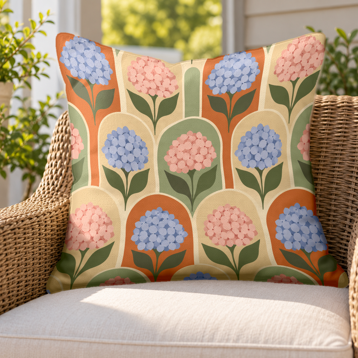 Terracotta hydrangea arch outdoor pillow on a rattan chair on a sunny porch