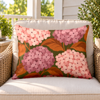 Blush hydrangea outdoor lumbar pillow on a rattan chair on a sunny porch