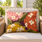 Plum mid-century hydrangea outdoor lumbar pillow on a rattan chair on a sunny porch