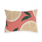 Modern outdoor lumbar pillow with cream citrus slices and dark green leaves on coral pink