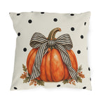 Orange pumpkin with a black and cream striped bow on a black polka dot outdoor pillow