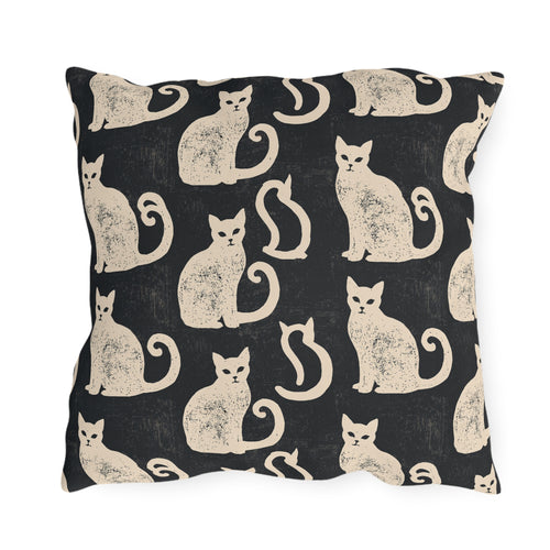 Cream folk art cats on a near-black outdoor pillow, worn block print