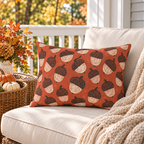 Block-printed acorn outdoor lumbar pillow in rust orange styled on a porch