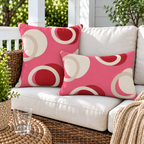 Pink and red modern circle outdoor pillow and matching outdoor lumbar pillow on a wicker porch sofa with cream cushions