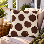 Brown and cream painted polka dot outdoor pillow on a porch armchair with a wicker side and green knit throw