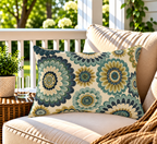 Teal and ochre folk flower outdoor lumbar pillow styled on a sunny porch