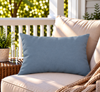 Solid dusty blue outdoor lumbar pillow styled on patio furniture