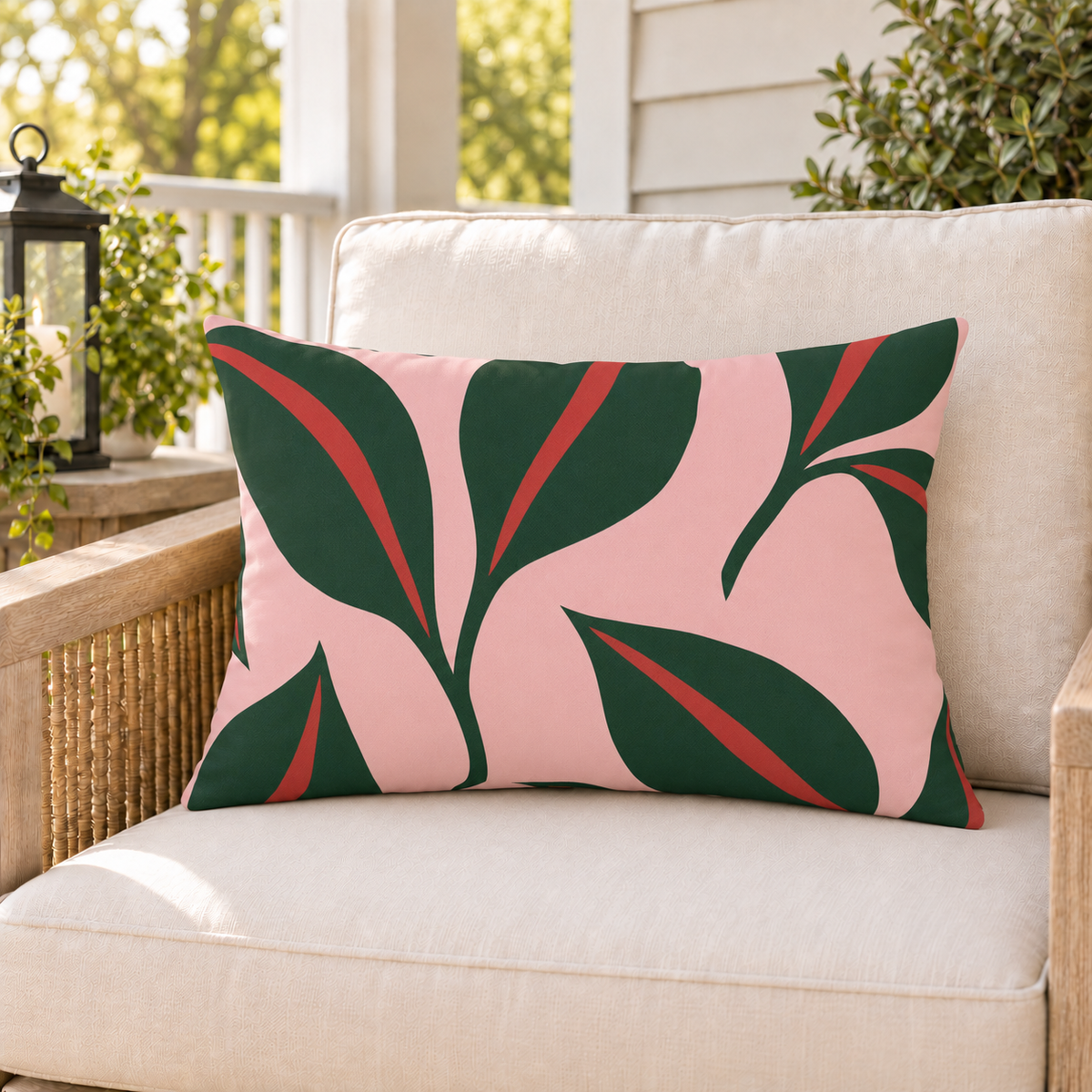 Pink and green leaf outdoor lumbar pillow styled on patio furniture