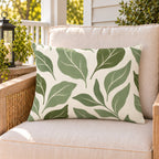 Sage green abstract leaf outdoor lumbar pillow on a rattan chair on a sunny summer porch