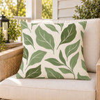 Sage green abstract leaf outdoor pillow on a rattan chair on a sunny summer porch