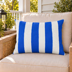 Blue and white awning stripe outdoor lumbar pillow on a rattan chair on a sunny summer porch
