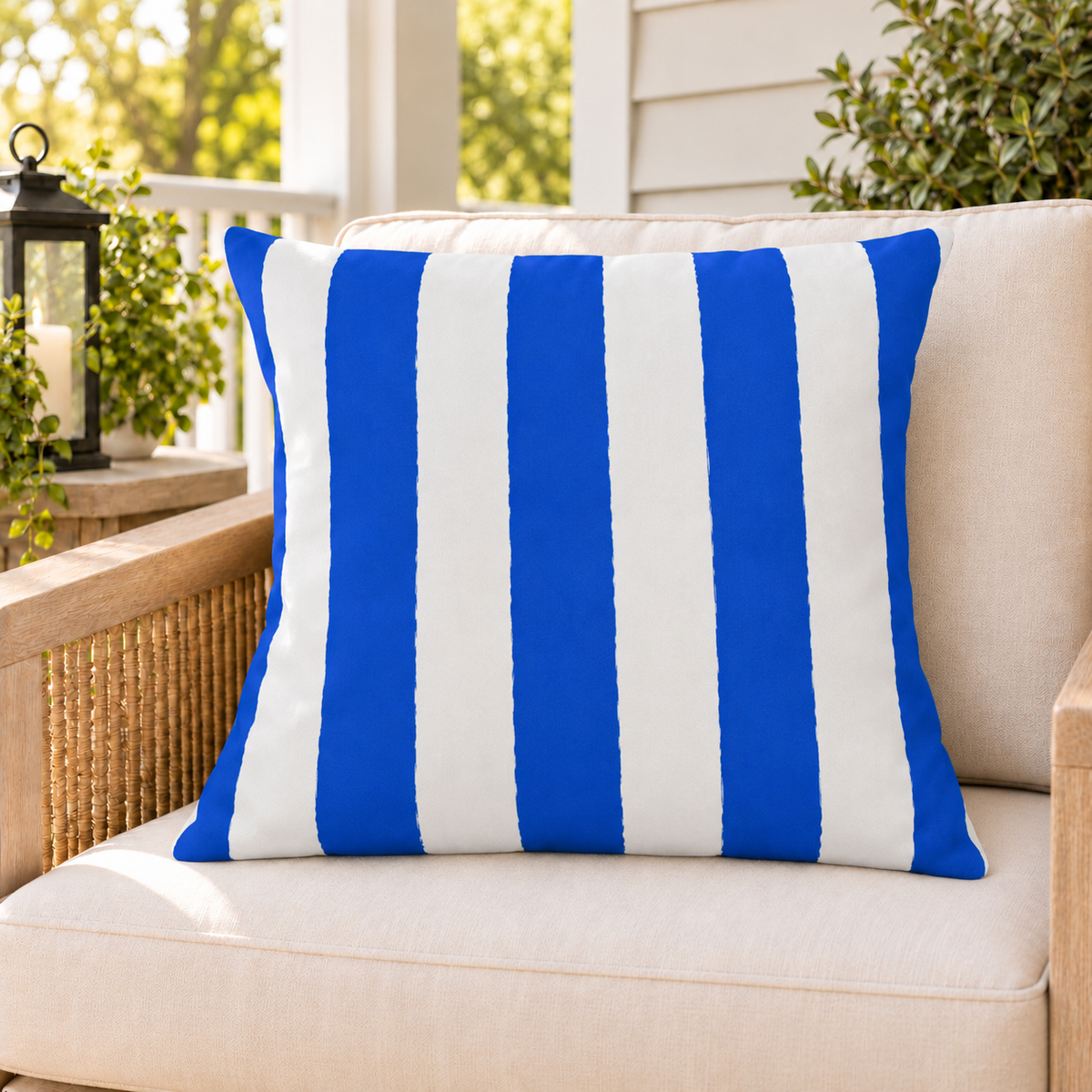 Blue and white awning stripe outdoor pillow on a rattan chair on a sunny summer porch