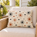 Boho sunburst outdoor lumbar pillow on a rattan chair on a sunny summer porch