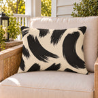 Black and cream brush stroke outdoor lumbar pillow on a rattan chair on a sunny summer porch