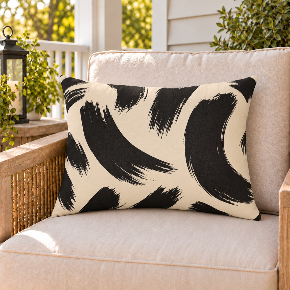 Black and cream brush stroke outdoor lumbar pillow on a rattan chair on a sunny summer porch