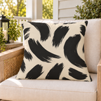Black and cream brush stroke outdoor pillow on a rattan chair on a sunny summer porch