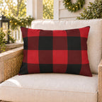 Red buffalo check outdoor lumbar pillow on a rattan porch chair with Christmas garland and warm lights