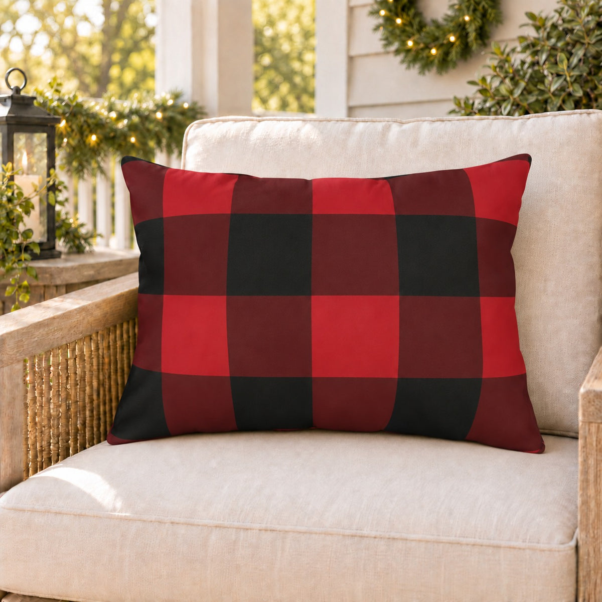 Red buffalo check outdoor lumbar pillow on a rattan porch chair with Christmas garland and warm lights