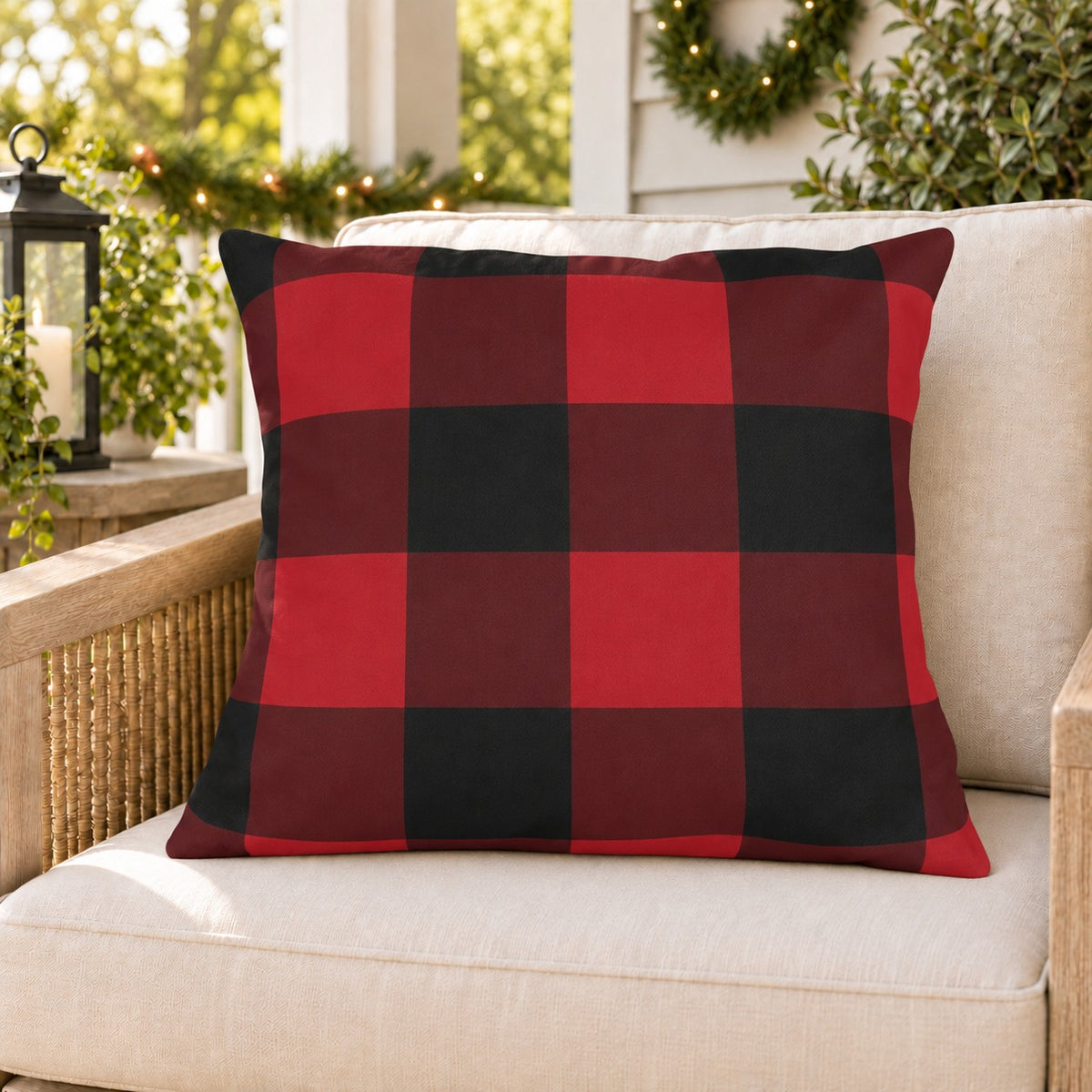 Red buffalo check outdoor pillow on a rattan porch chair with Christmas garland and warm lights