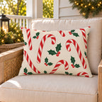 Red candy cane Christmas outdoor lumbar pillow on a rattan chair on a cozy holiday porch decorated with greenery and lights