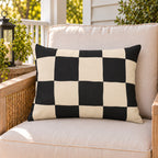 Black and cream checkerboard outdoor lumbar pillow on a rattan chair on a sunny summer porch