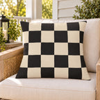 Black and cream checkerboard outdoor pillow on a rattan chair on a sunny summer porch