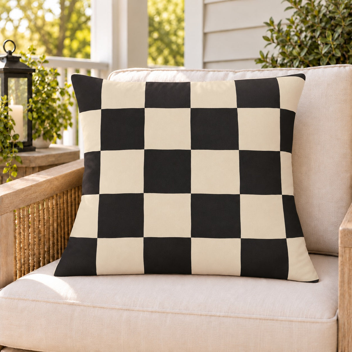 Black and cream checkerboard outdoor pillow on a rattan chair on a sunny summer porch