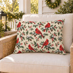 Cream Christmas cardinal outdoor lumbar pillow on a rattan porch chair with Christmas garland and warm lights