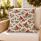 Cream Christmas cardinal outdoor pillow on a rattan porch chair with Christmas garland and warm lights
