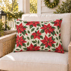 Red Christmas poinsettia outdoor lumbar pillow on a rattan porch chair with Christmas garland and warm lights