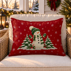 Red Christmas snowman outdoor lumbar pillow on a rattan chair on a snowy Christmas porch