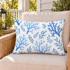 Blue coral coastal outdoor lumbar pillow on a rattan chair on a sunny summer porch