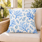 Blue coral coastal outdoor pillow on a rattan chair on a sunny summer porch