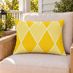 Yellow harlequin diamond outdoor lumbar pillow on a rattan chair on a sunny summer porch