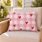 Heart Gingham Pink outdoor lumbar pillow on a rattan chair on a sunny summer porch