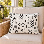Black and white mudcloth outdoor lumbar pillow on a rattan chair on a sunny summer porch