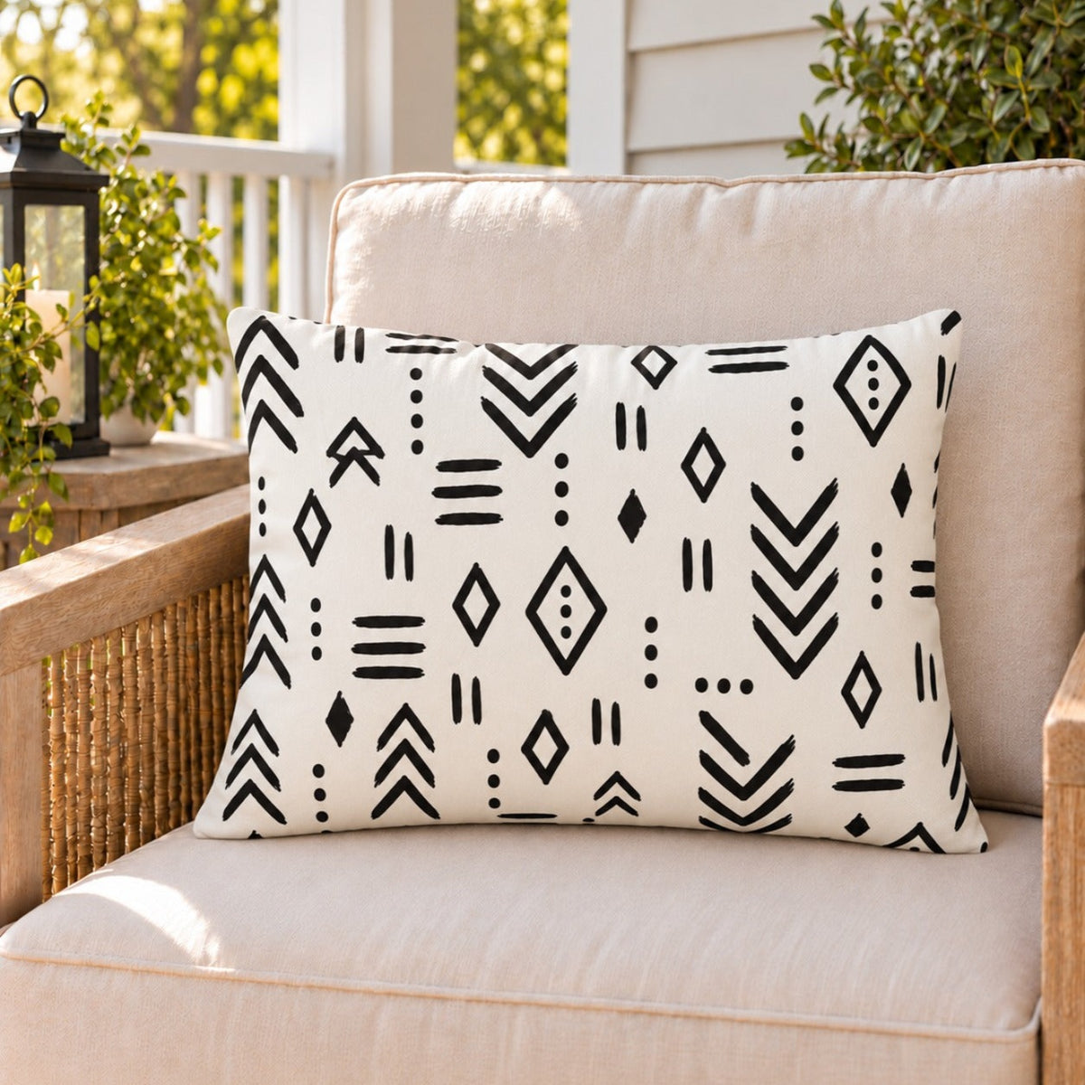 Black and white mudcloth outdoor lumbar pillow on a rattan chair on a sunny summer porch