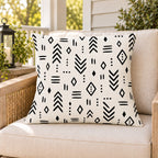 Black and white mudcloth outdoor pillow on a rattan chair on a sunny summer porch