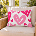 Painted Heart Hot Pink outdoor lumbar pillow on a rattan chair on a sunny summer porch